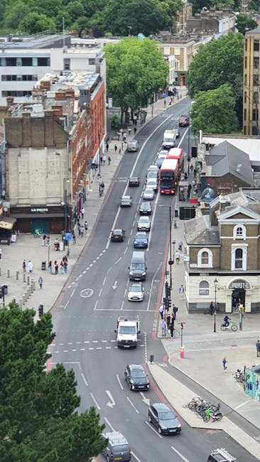 A view of a city street with a tall historic clock tower in the background, part of a larger building complex with domed structures. In the foreground, an empty road curves gently to the right, with v
